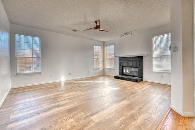 unfurnished living room with a ceiling fan, visible vents, a fireplace, a textured ceiling, and light wood-type flooring