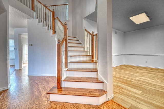 stairway with visible vents, wood finished floors, baseboards, and a textured ceiling