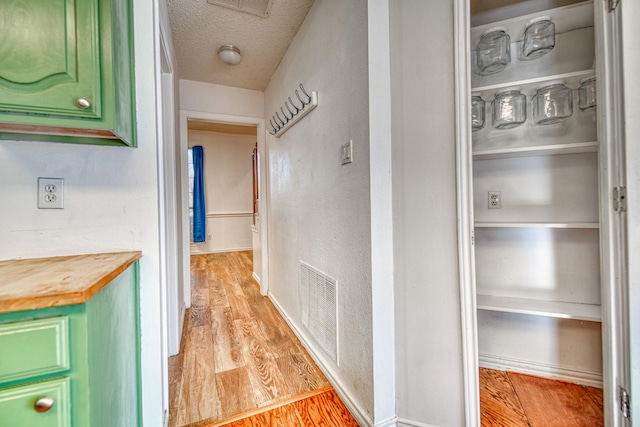 corridor featuring light wood finished floors, visible vents, and a textured ceiling