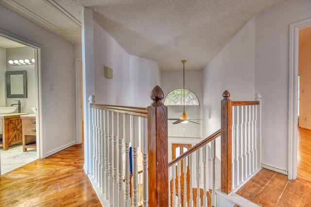 corridor featuring an upstairs landing, a sink, a textured ceiling, wood finished floors, and baseboards