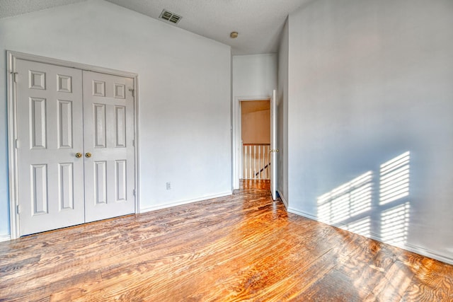 unfurnished bedroom with visible vents, a textured ceiling, wood finished floors, a closet, and lofted ceiling