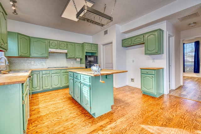 kitchen with a sink, black appliances, light wood-type flooring, backsplash, and butcher block counters