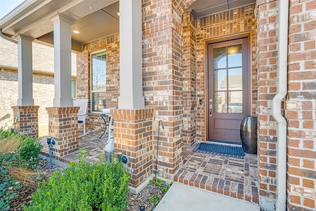 view of exterior entry with a porch and brick siding