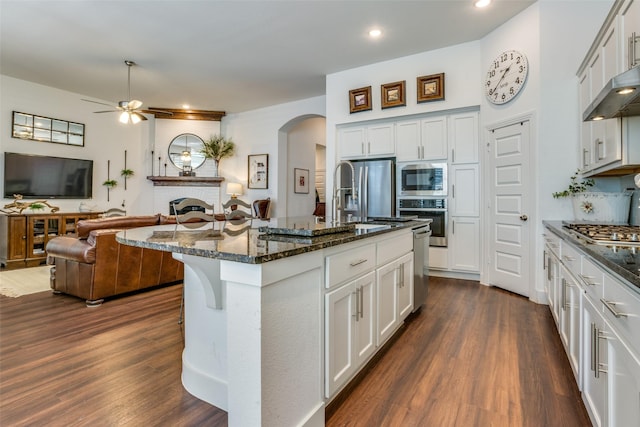 kitchen featuring stainless steel appliances, an island with sink, white cabinetry, and dark stone counters