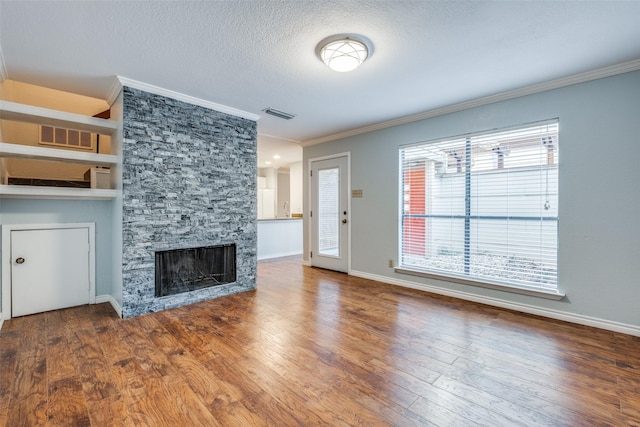 unfurnished living room featuring a textured ceiling, crown molding, built in features, wood-type flooring, and a stone fireplace