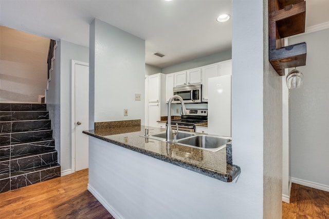 kitchen with appliances with stainless steel finishes, white cabinets, kitchen peninsula, and wood-type flooring