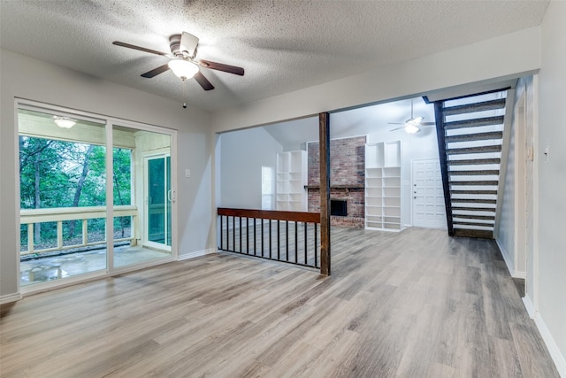 unfurnished room with a textured ceiling, ceiling fan, light wood-type flooring, and a fireplace