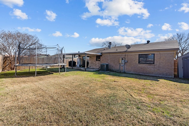 rear view of property with cooling unit, a storage shed, a trampoline, and a lawn