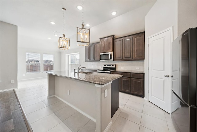 kitchen with decorative light fixtures, an island with sink, dark brown cabinets, light stone countertops, and appliances with stainless steel finishes