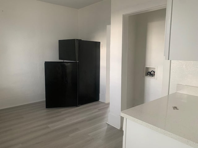 kitchen with black refrigerator, white cabinetry, and light hardwood / wood-style floors