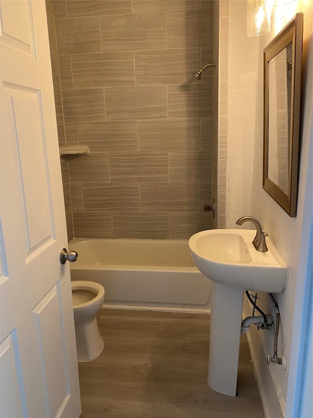 bathroom featuring toilet, tiled shower / bath, and wood-type flooring