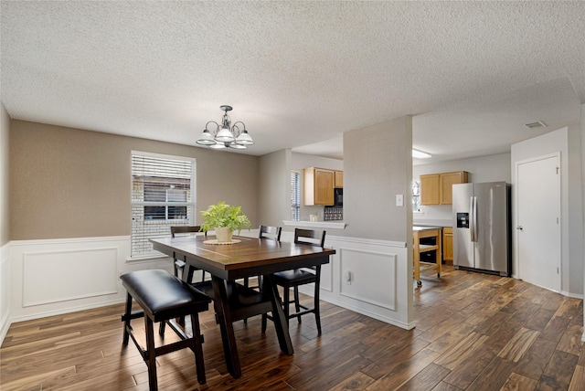 dining area with an inviting chandelier, a textured ceiling, and dark wood-type flooring