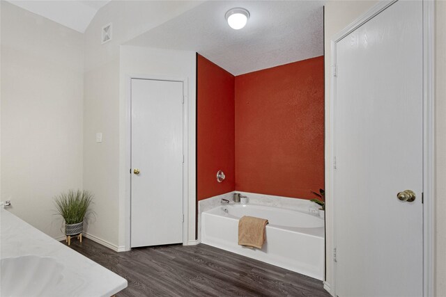 bathroom featuring a tub, a textured ceiling, vaulted ceiling, and wood-type flooring