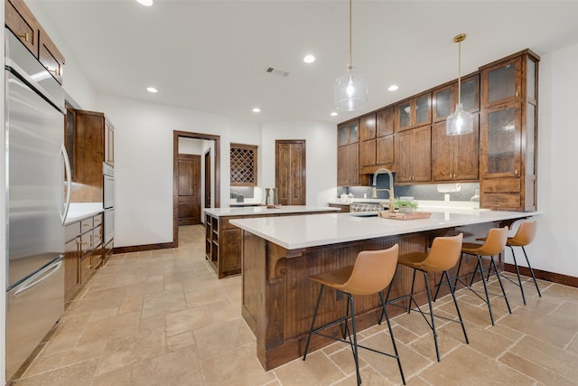 kitchen featuring built in fridge, sink, pendant lighting, and a kitchen bar