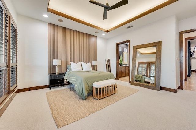 carpeted bedroom featuring ceiling fan, ensuite bathroom, and a tray ceiling