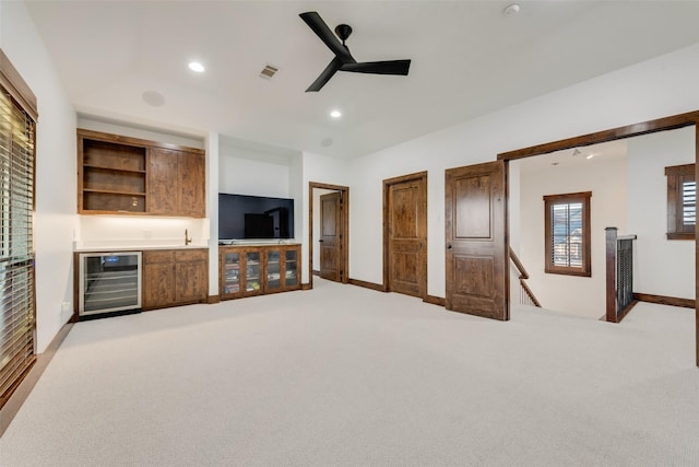 unfurnished living room featuring light carpet, ceiling fan, beverage cooler, and bar