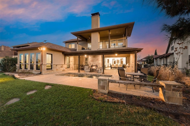 back house at dusk with a balcony, a patio area, and a yard