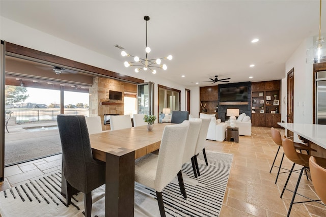 dining space featuring ceiling fan with notable chandelier, a stone fireplace, and built in shelves