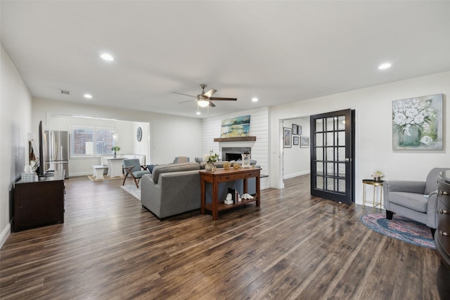 living room featuring ceiling fan, a large fireplace, and dark hardwood / wood-style floors