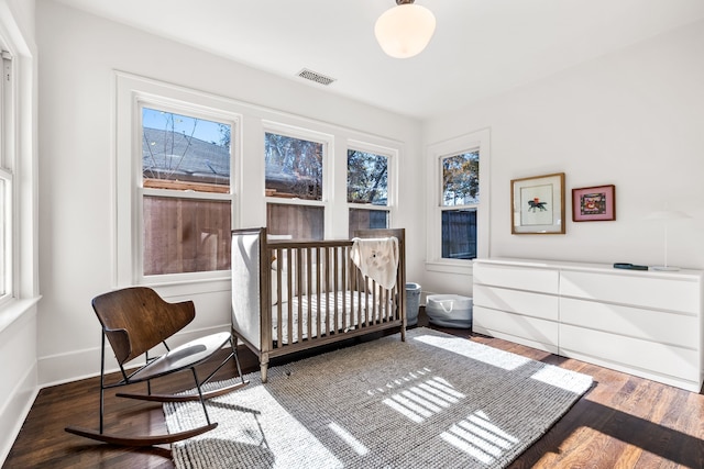 bedroom featuring multiple windows, a crib, and dark hardwood / wood-style floors