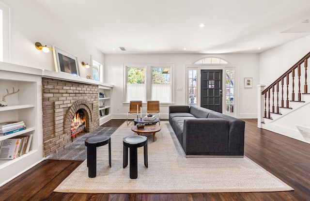 living room with dark hardwood / wood-style flooring, a brick fireplace, and built in shelves