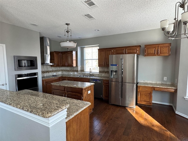 kitchen featuring stainless steel appliances, light stone countertops, a kitchen island, wall chimney range hood, and pendant lighting