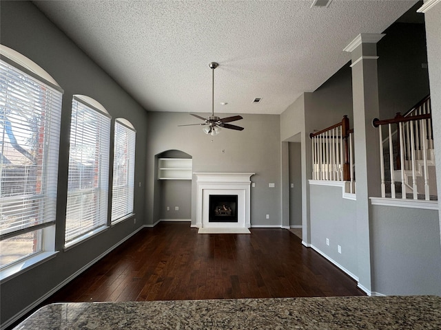 unfurnished living room featuring dark wood-type flooring, a textured ceiling, ceiling fan, and ornate columns