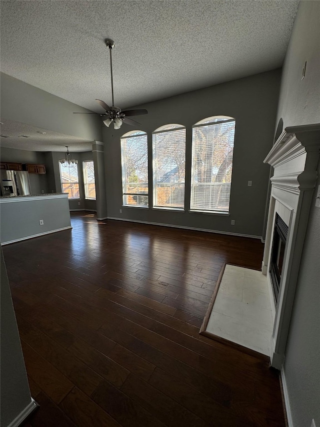 unfurnished living room with a textured ceiling, dark hardwood / wood-style floors, a tile fireplace, and ceiling fan with notable chandelier