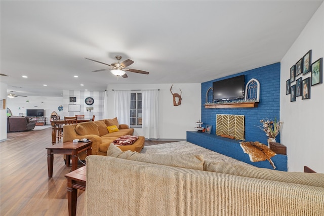 living room featuring ceiling fan, a fireplace, and wood-type flooring