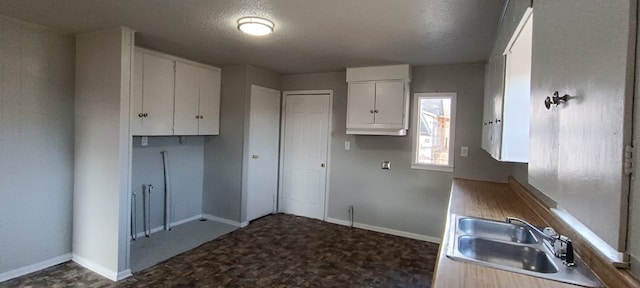 kitchen with sink, white cabinets, a textured ceiling, and dark carpet