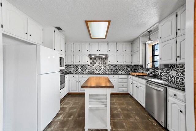 kitchen with wood counters, white cabinetry, appliances with stainless steel finishes, a kitchen island, and sink