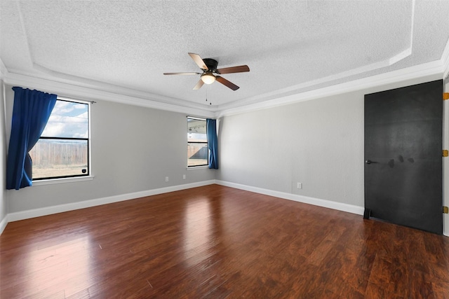 empty room with a raised ceiling, ceiling fan, dark hardwood / wood-style floors, and plenty of natural light