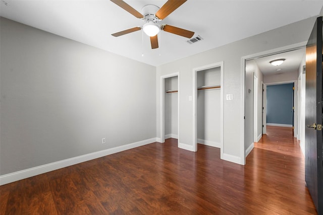 unfurnished bedroom featuring ceiling fan, dark hardwood / wood-style flooring, and two closets