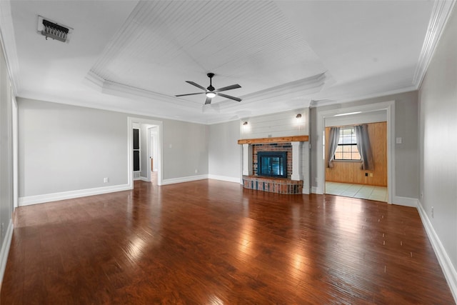 unfurnished living room with ceiling fan, a brick fireplace, a tray ceiling, wood-type flooring, and ornamental molding