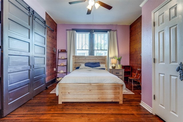 bedroom with ceiling fan, dark wood-type flooring, a barn door, and wood walls