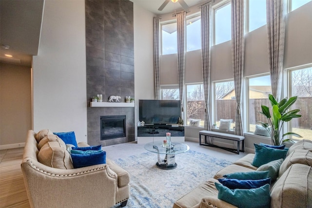 living room featuring a healthy amount of sunlight, ceiling fan, a fireplace, and a high ceiling