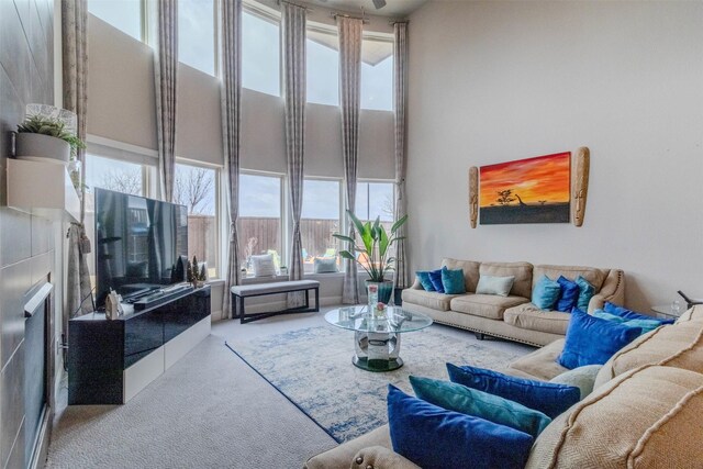 living room with a towering ceiling, carpet flooring, and a tiled fireplace