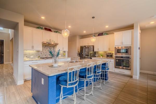 kitchen featuring sink, decorative light fixtures, an island with sink, stainless steel appliances, and white cabinets