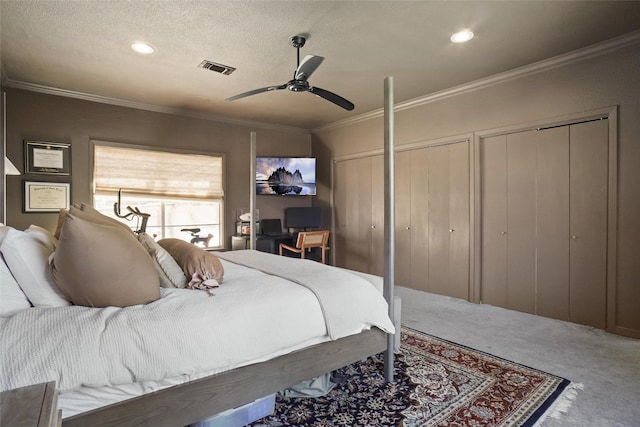 carpeted bedroom with ceiling fan, two closets, a textured ceiling, and ornamental molding