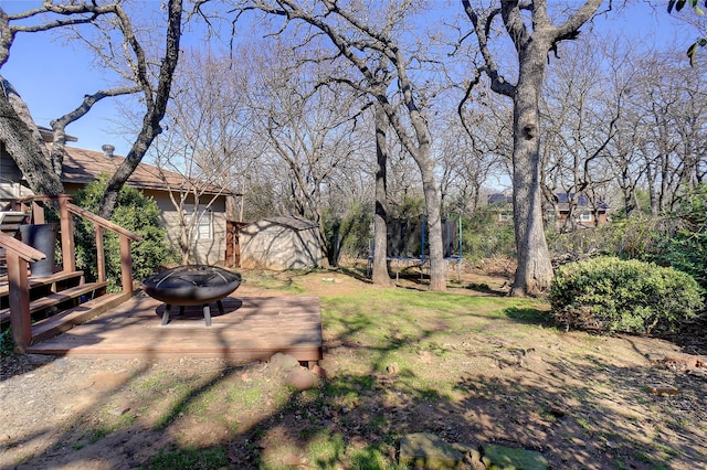 view of yard with a wooden deck, an outdoor fire pit, and a trampoline