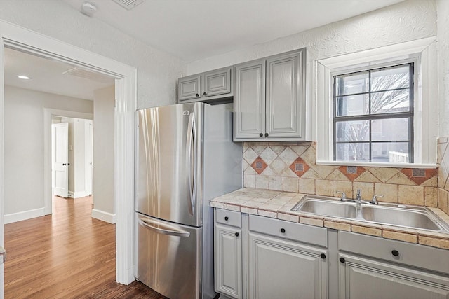 kitchen with gray cabinets, stainless steel fridge, decorative backsplash, hardwood / wood-style flooring, and sink