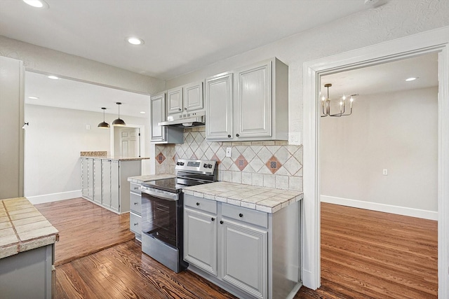 kitchen featuring dark wood-type flooring, tile countertops, hanging light fixtures, stainless steel electric stove, and tasteful backsplash