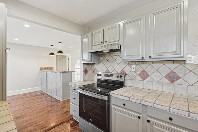 kitchen featuring tile countertops, hardwood / wood-style floors, decorative backsplash, hanging light fixtures, and stainless steel range with electric stovetop