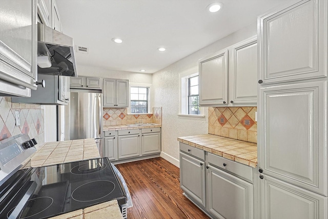 kitchen with tile counters, dark hardwood / wood-style floors, stainless steel appliances, tasteful backsplash, and sink