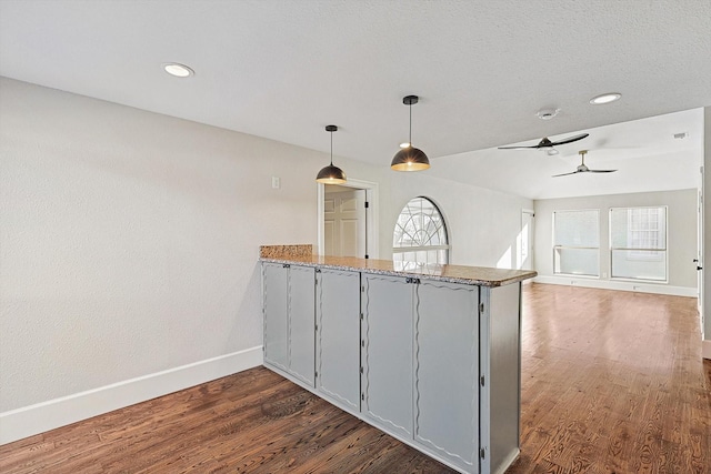 kitchen with stone counters, ceiling fan, kitchen peninsula, dark hardwood / wood-style flooring, and pendant lighting