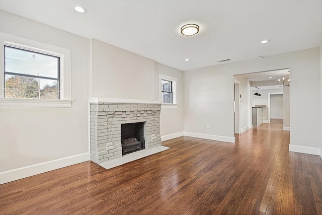 unfurnished living room featuring a healthy amount of sunlight, a brick fireplace, and hardwood / wood-style flooring