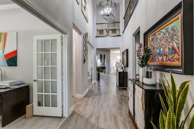 corridor featuring a towering ceiling, a notable chandelier, light hardwood / wood-style floors, and crown molding