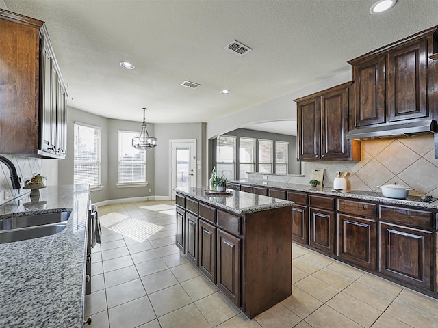 kitchen featuring black electric cooktop, light stone counters, a kitchen island, sink, and dark brown cabinets