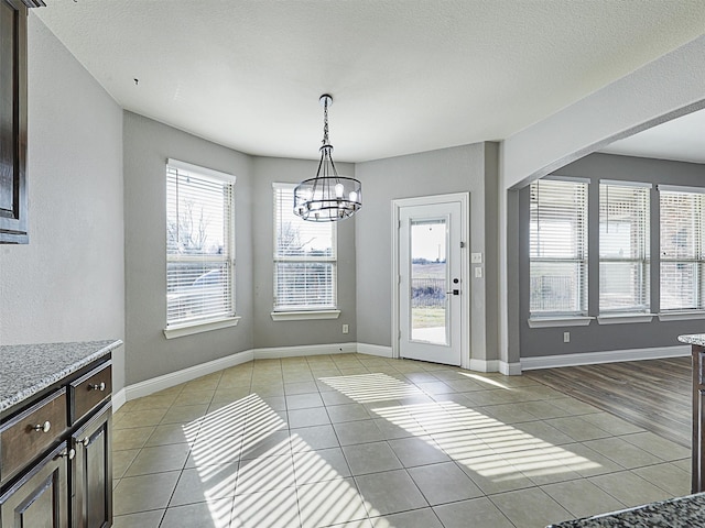 unfurnished dining area featuring a textured ceiling, light tile patterned floors, and a chandelier