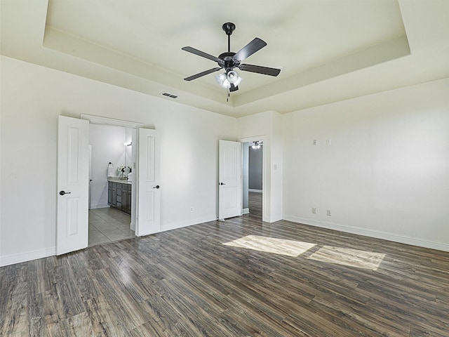 unfurnished bedroom with a raised ceiling, ceiling fan, and connected bathroom